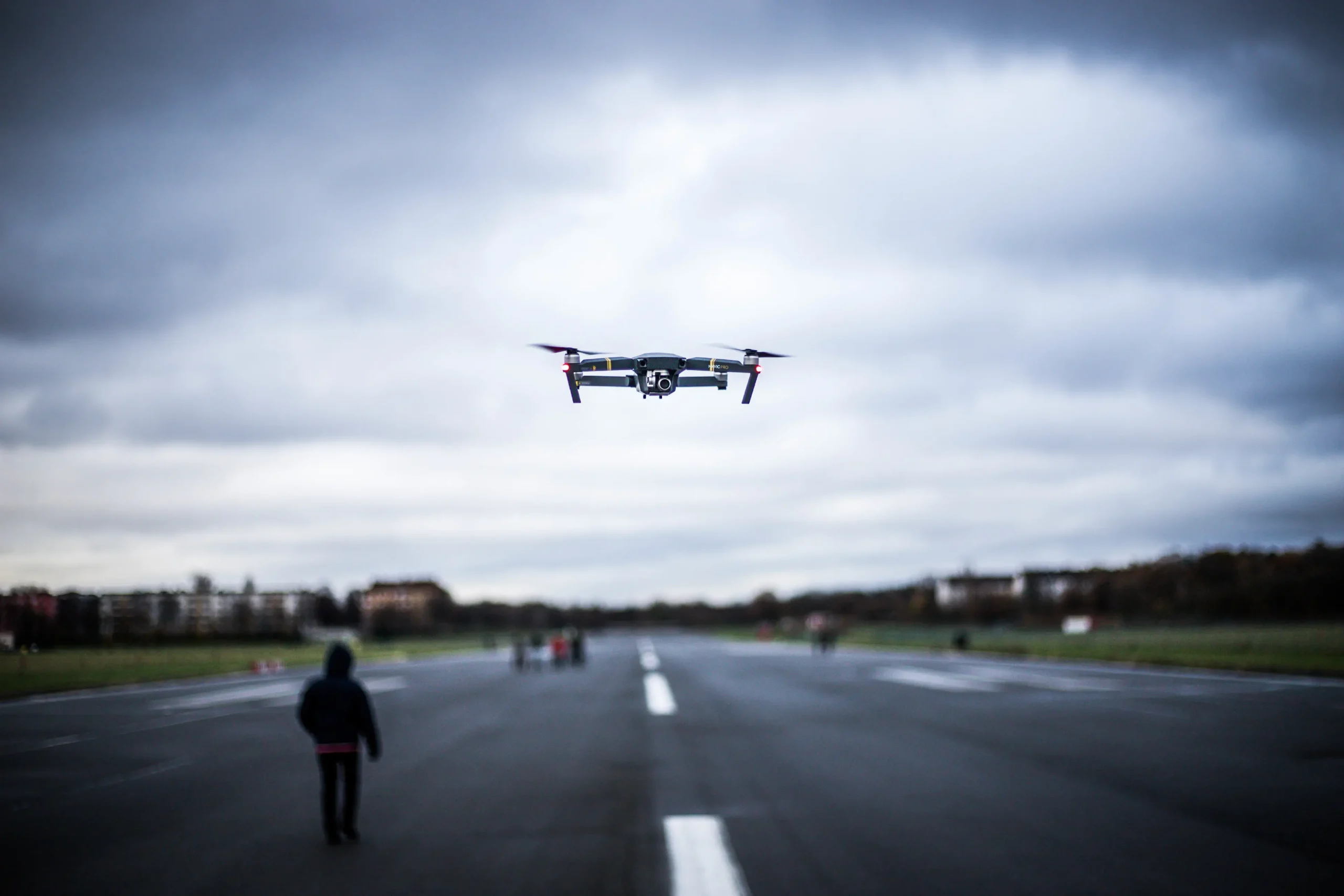 Drone flying above runway with blurry people in the distance and moody sky